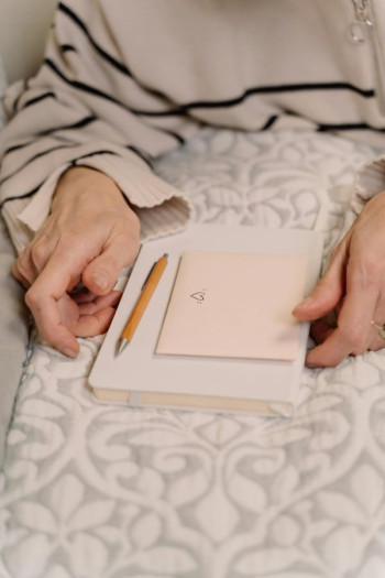 A person's hand is seen resting near a blank notebook and letter and pen.